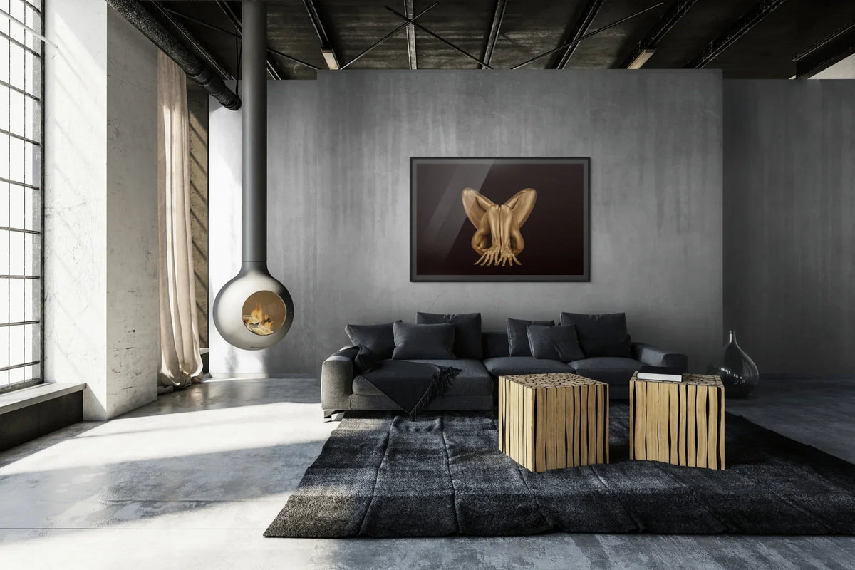 Fine art print by Zack Zublena featuring a golden body sculpture in a symmetrical pose, displayed above a dark sofa on a textured grey wall in a loft space