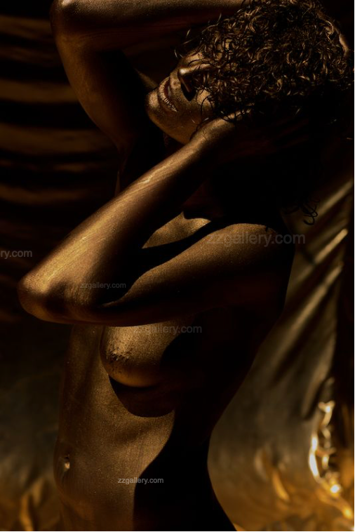 Golden-painted silhouette with curly hair arching gracefully, hands lifted behind her head, bathed in dramatic light and shadows. Fine art photography capturing elegance, feminine strength, and timeless beauty, perfect for luxury interiors and collectors.