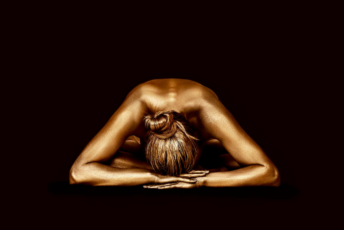 Figura femminile dorata nella posa di un bambino: fotografia artistica che simboleggia riposo, relax e serenità. Sfondo scuro con corpo dorato radioso, perfetto per spa, yoga o decorazioni da parete per il benessere.