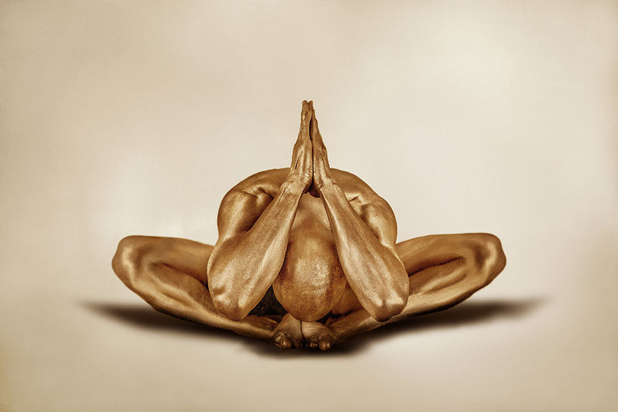 Golden-painted male figure in a meditative yoga pose with hands pressed together, displayed as fine art wall décor in a modern living room interior.