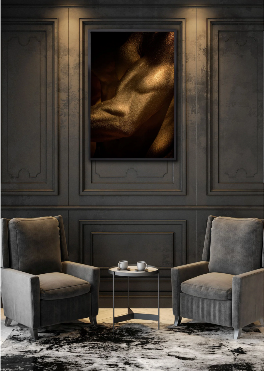 Golden male torso fine art photograph displayed in a refined dark interior with two armchairs, modern wall paneling, and soft spotlighting.