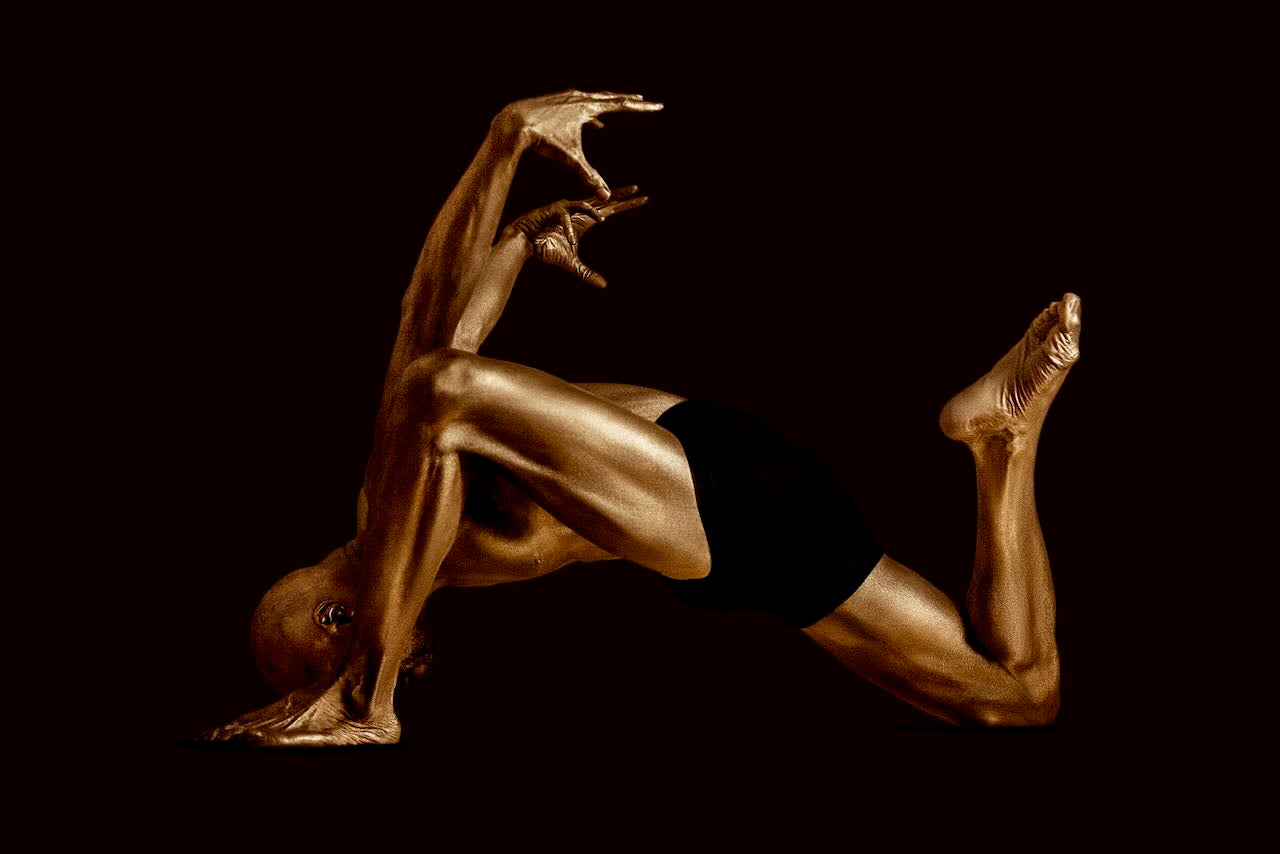 Golden-painted male form in dynamic bull yoga pose, sculptural fine art photography highlighting strength and balance, luxury wall decor for spas, yoga studios, and modern interiors.