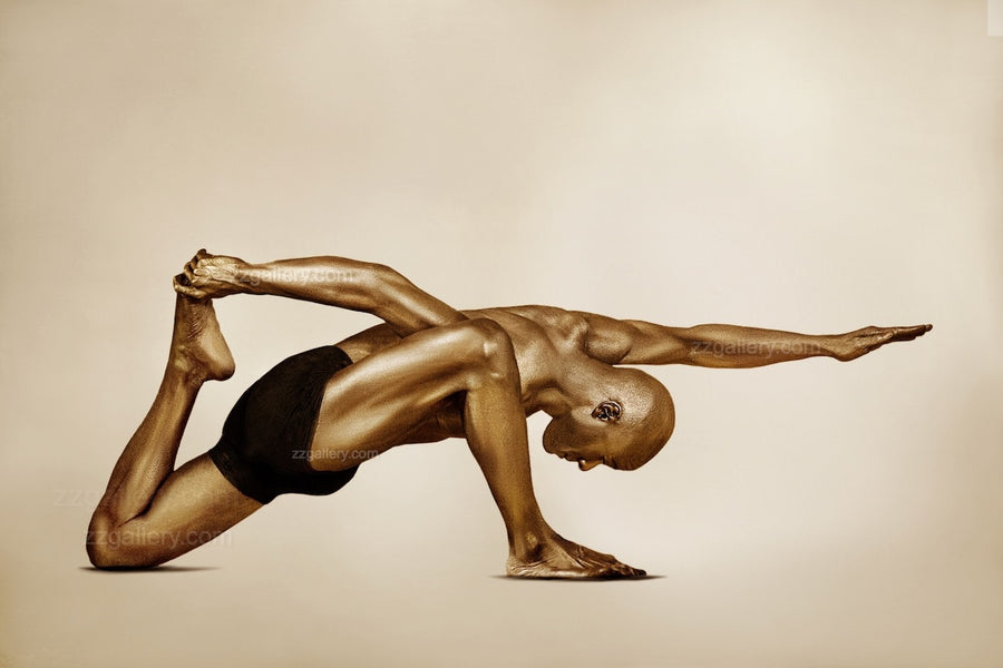 Golden-painted male figure in a powerful yoga balance pose by Zack Zublena, with one arm extended forward and the other gripping the foot, symbolizing strength, focus, and body-mind harmony.