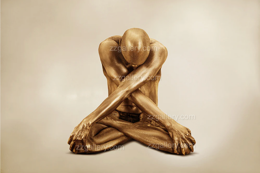 Golden-painted male figure seated cross-legged with arms crossed, displayed as fine art wall decor in a modern living room interior.