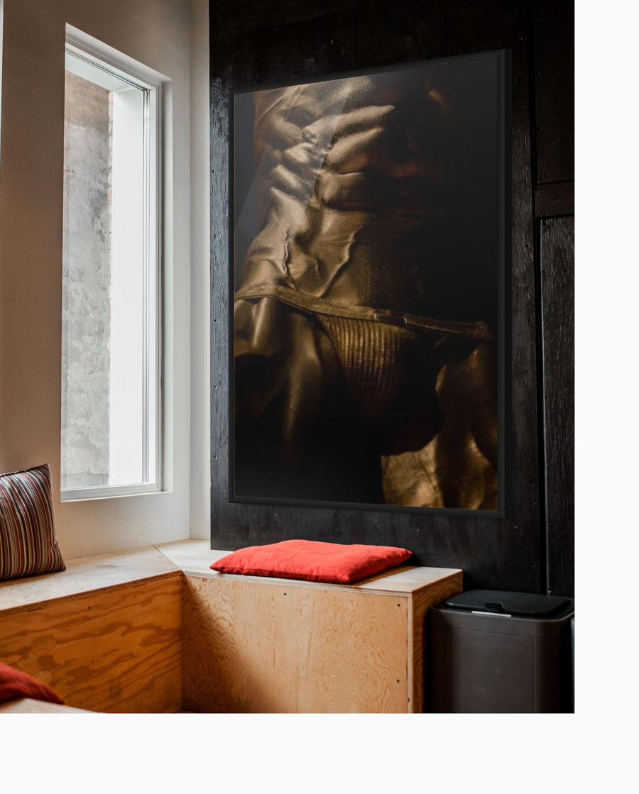 Golden muscular male abs and torso fine art print displayed in a modern interior with wood and cushions, luxury wall art for collectors, gym inspiration, wellness spaces, and contemporary design.