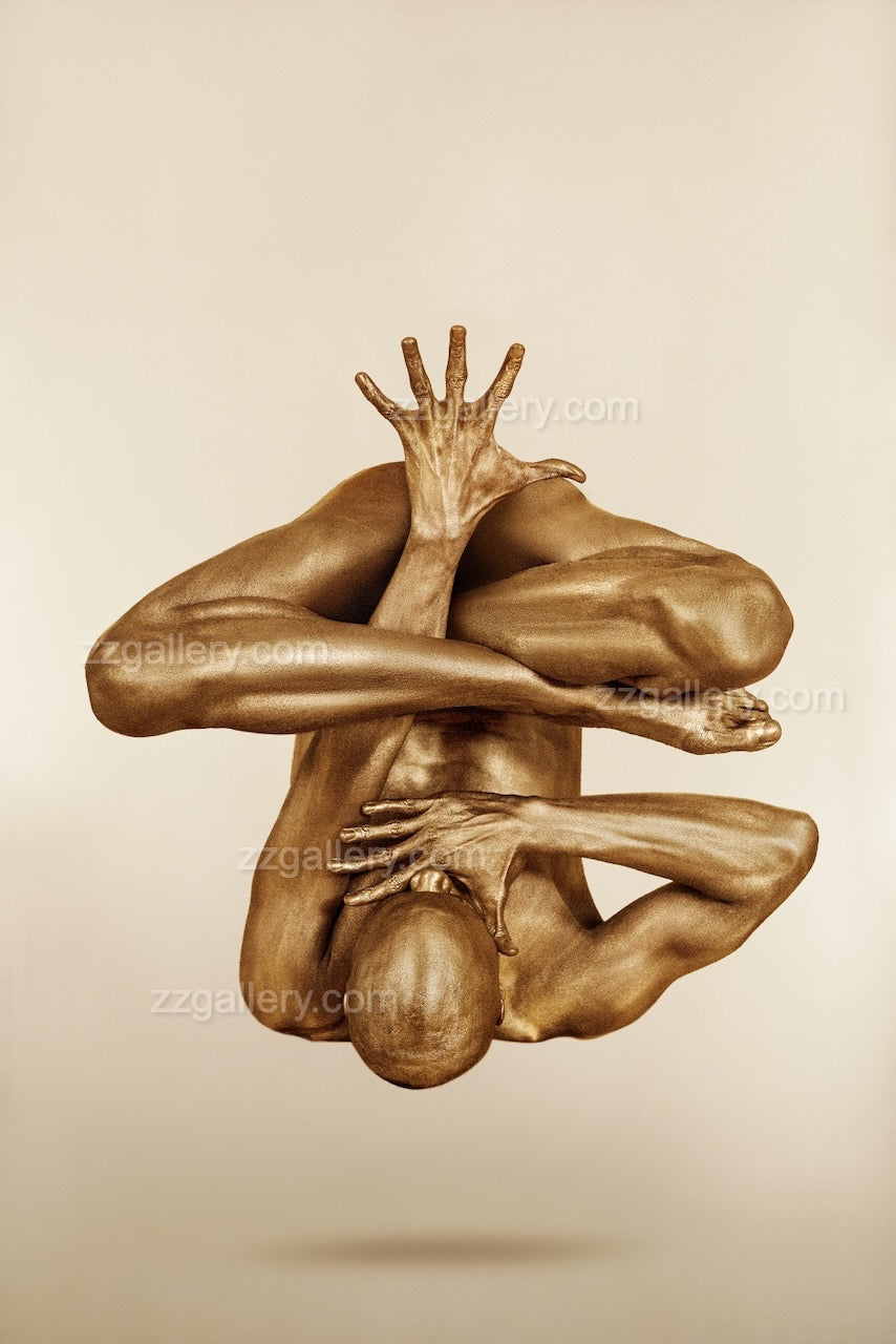 Golden body art photography of a suspended yoga pose, featuring a painted yogi in mid-air balance with arms folded and one hand extended upward. Contemporary fine art wall decor by Zack Zublena, ideal for modern interiors, yoga studios, and wellness spaces.