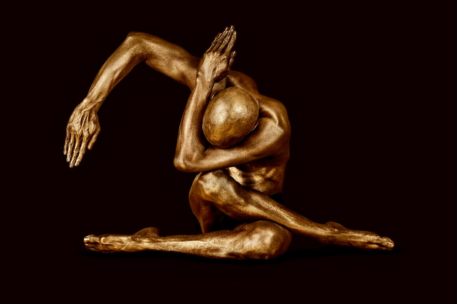 Golden-painted male figure in a sculptural seated yoga pose with extended arm, fine art photography by Zack Zublena from the Dark Elegance collection.