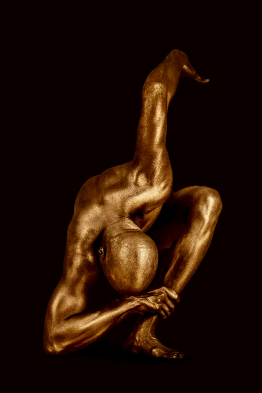 Contemporary fine art photography by Zack Zublena featuring a gold-painted figure in a dramatic forward bend with one leg lifted, embodying strength, balance, and modern sculptural elegance on a moody dark background. Perfect for luxury wall decor and wellness-inspired interiors.