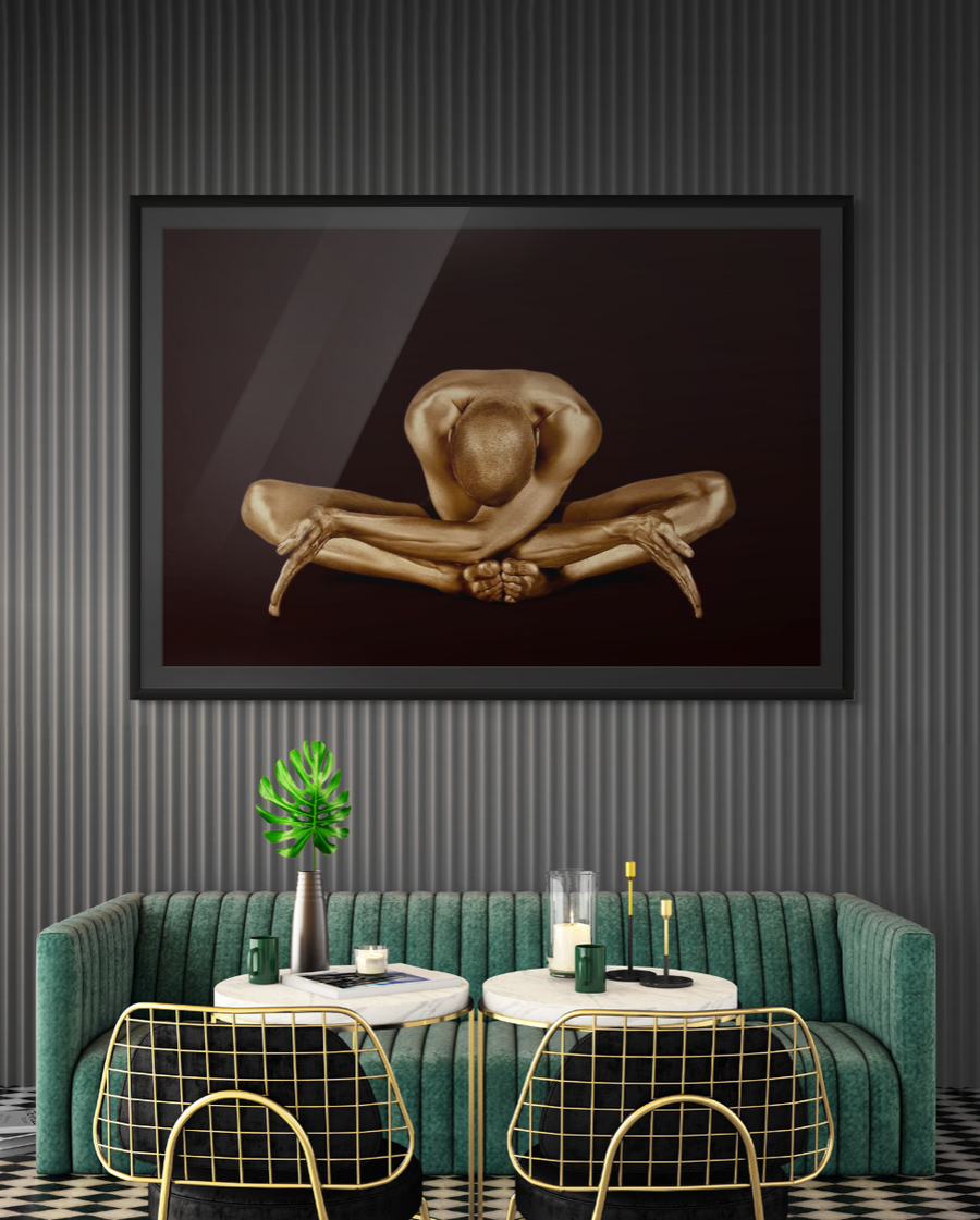 Golden-painted male figure in a deep yoga stretch with head bowed forward, captured against a black background. Fine art photography by Zack Zublena for luxury wall décor in modern interiors.