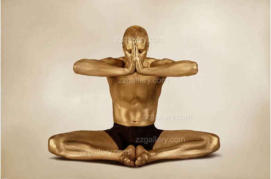 Golden-painted male figure seated in a cross-legged meditation pose with arms extended in prayer, captured in conceptual fine art photography for luxury wall decor.