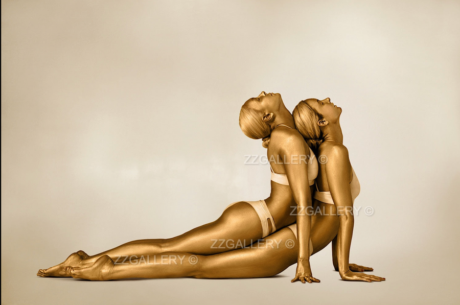 Fine art photograph of two golden-painted women in a mirrored yoga pose, symbolizing unity, balance, and fluidity. Perfect wall art for yoga studios, wellness centers, luxury interiors, and collectors of contemporary gold photography.