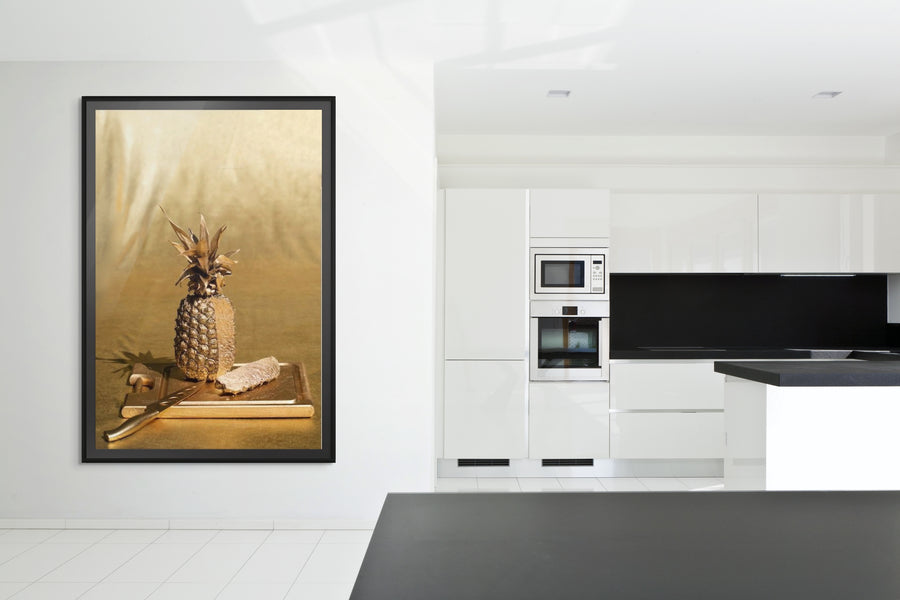 Golden pineapple fine art photograph by Zack Zublena, displayed in a modern white kitchen, blending playful luxury with culinary-inspired wall décor.