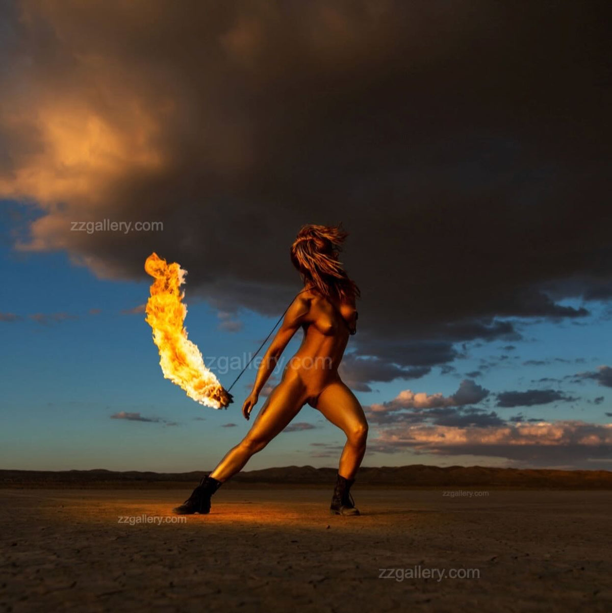 Golden-painted dancer captured mid-motion with blazing torch against dramatic desert sunset sky — fine art fire photography.