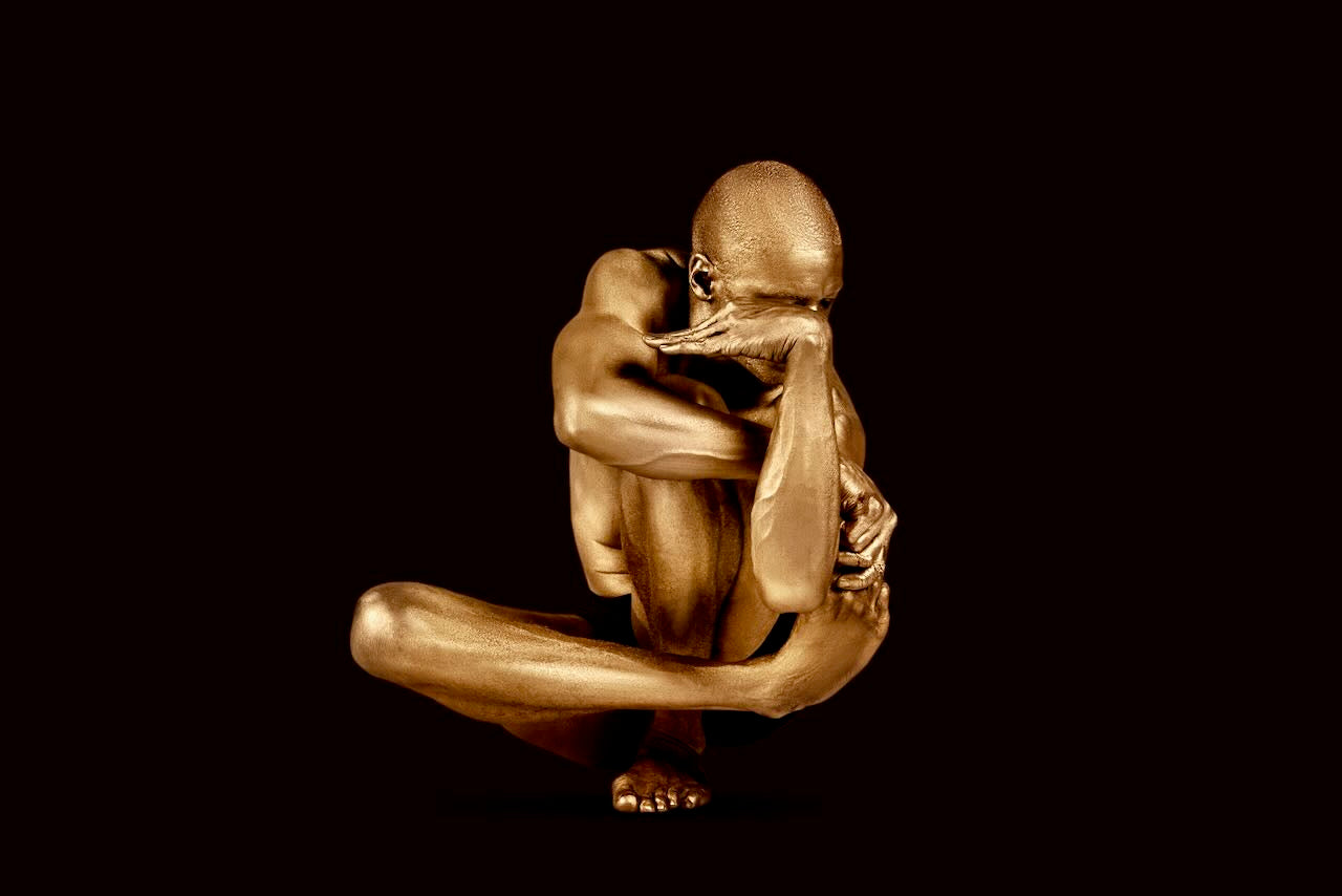 Golden-painted male figure in a sculptural seated pose with arms and legs intertwined, fine art wall decor for meditation rooms, luxury interiors, and collectors.