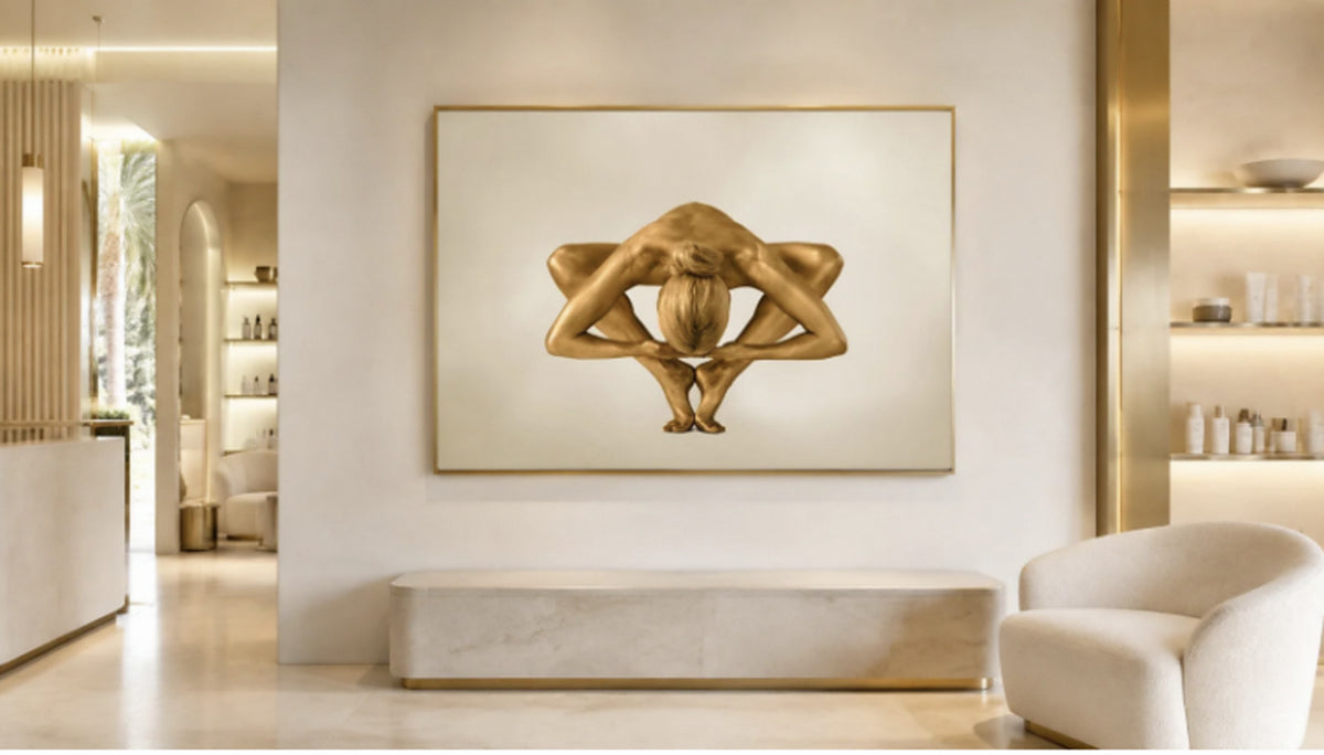 Supernova, gold body paint fine art photograph by Zack Zublena, framed in a cream and brass luxury spa lobby with a travertine bench and ivory armchair