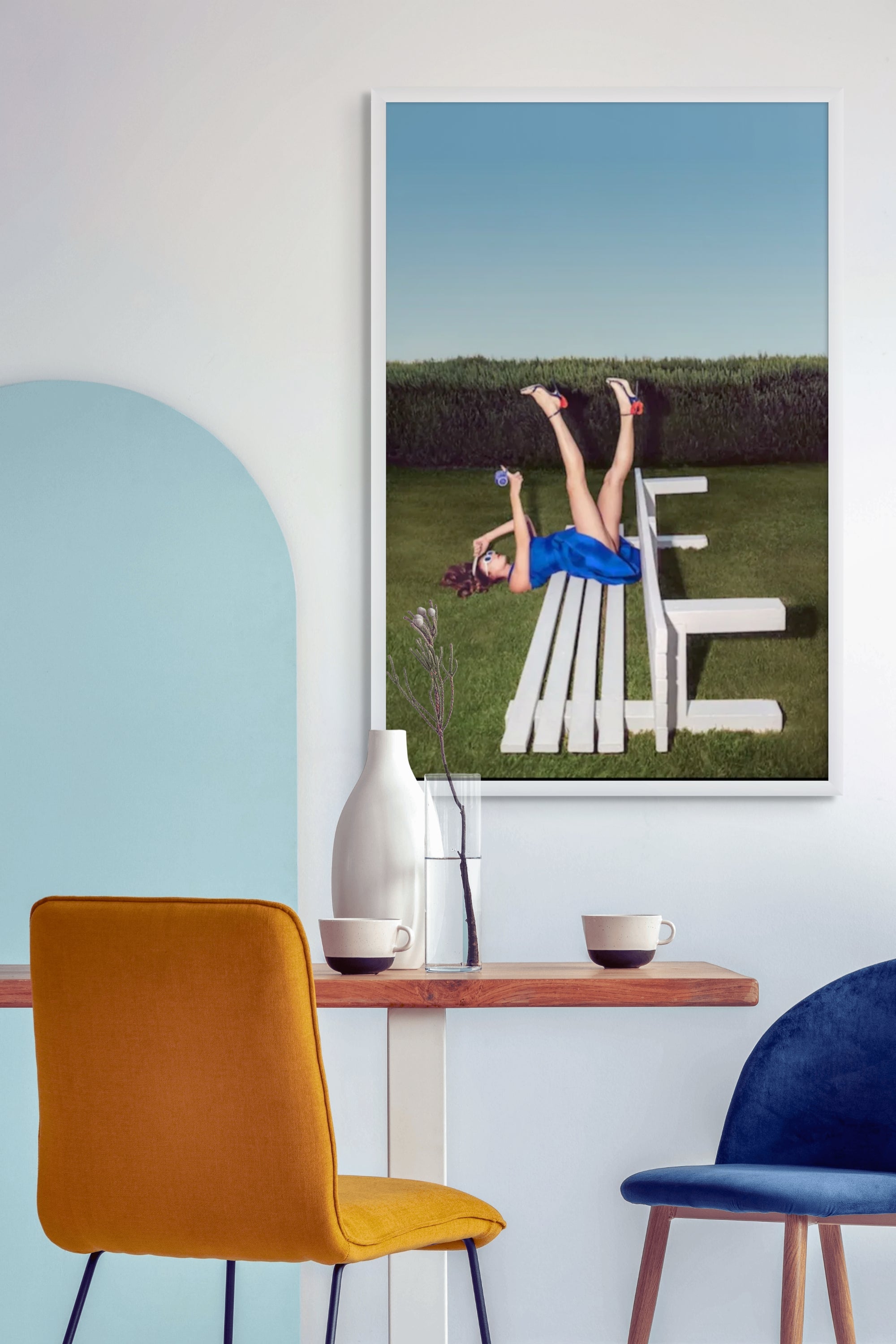 Surreal fine art wall art by Zack Zublena from the ‘Dazed of Our Lives’ collection, featuring a woman in a vibrant blue dress playfully posed upside down on a white bench against a clear sky background.”