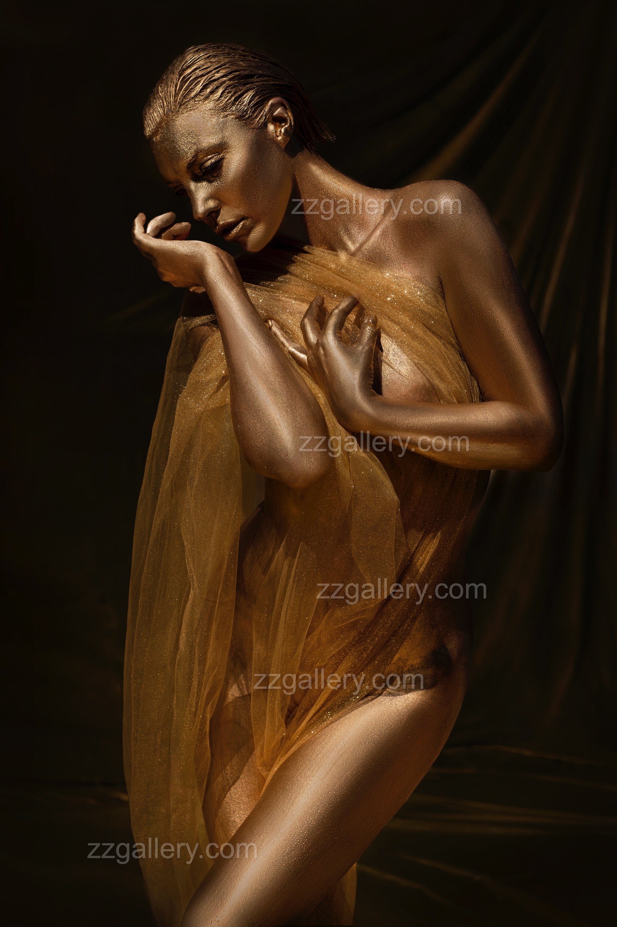 Golden-painted female figure with closed eyes, draped in sheer fabric, posed gracefully in a serene and elegant composition.