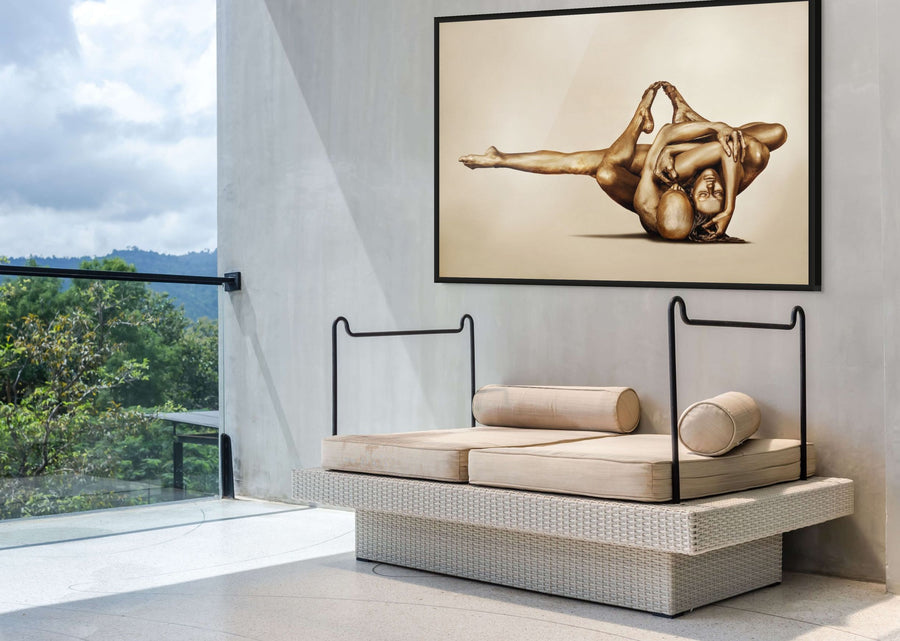 Golden-painted couple in an intertwined acrobatic yoga pose, captured as fine art wall photography and displayed in a modern outdoor lounge with mountain views.