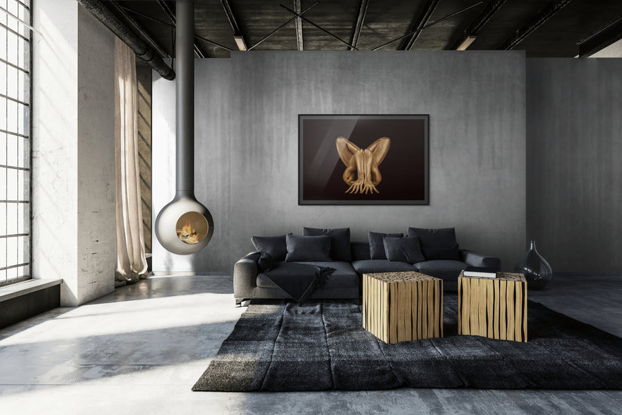 Contemporary golden nude fine art photography in a dramatic pose, displayed in a sleek industrial living room with concrete walls, hanging fireplace, and modern minimalist furniture. Edgy statement wall art for collectors and luxury interiors.