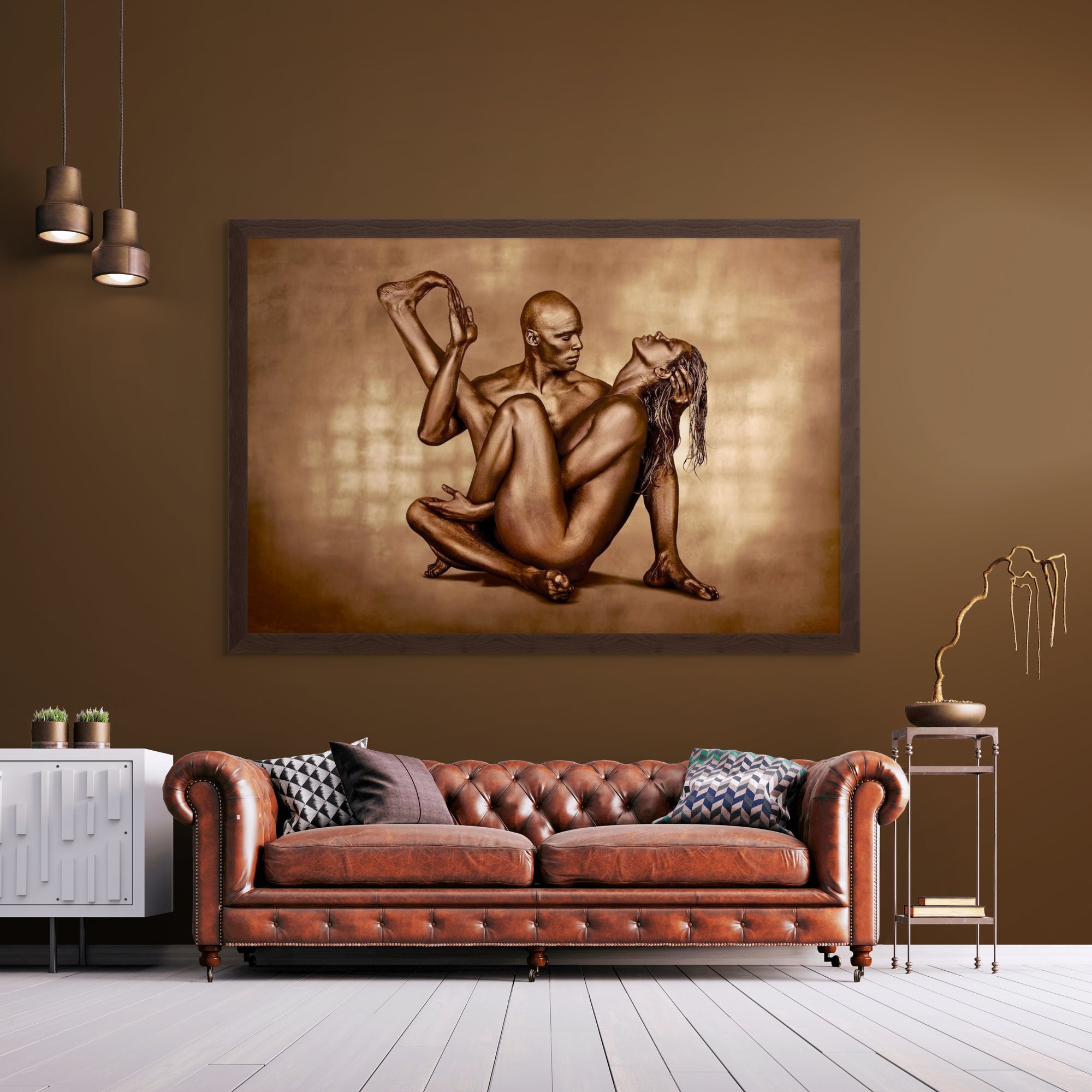 Golden-painted couple in a seated intertwined pose, captured as fine art wall photography by Zack Zublena and displayed in a modern living room with a leather sofa and warm brown tones.
