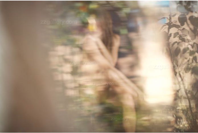 Abstract fine art photograph of a golden-painted feminine figure, softened by natural reflections and soft focus, surrounded by foliage and light.