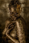 Close-up fine art photograph of a gold-painted nude woman with leopard skin patterns and ornate golden mask, symbolizing primal beauty and feminine power.
