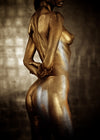 Side-back view of gold and silver-painted female body in elegant pose, fine art photo capturing sacred feminine energy and form, side nipple