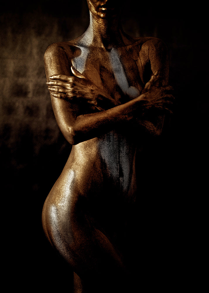 Gold-painted nude female figure with arms crossed over chest, fine art photography expressing feminine strength, protection, and sacred energy
