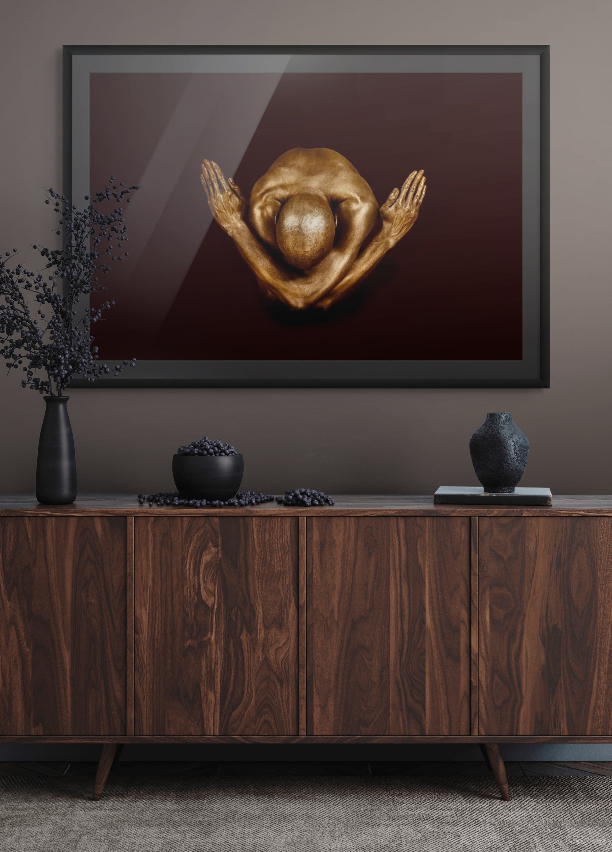 Golden-painted male figure in a crossed-arms yogi pose against a deep dark backdrop, framed as fine art wall decor in a modern luxury interior.