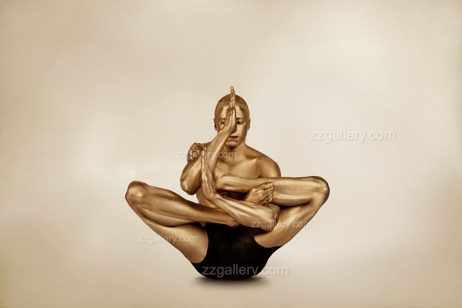 Golden-painted male figure in advanced yoga pose, fine art photograph displayed as framed wall art above a modern wooden shelf with black vases.