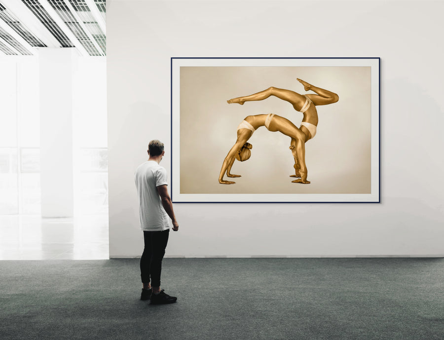 Golden-painted female duo in an acrobatic yoga arch pose, captured as contemporary fine art wall décor. An elegant composition emphasizing balance, harmony, and feminine strength. Perfect for luxury interiors, yoga studios, wellness spaces, and modern art collectors.