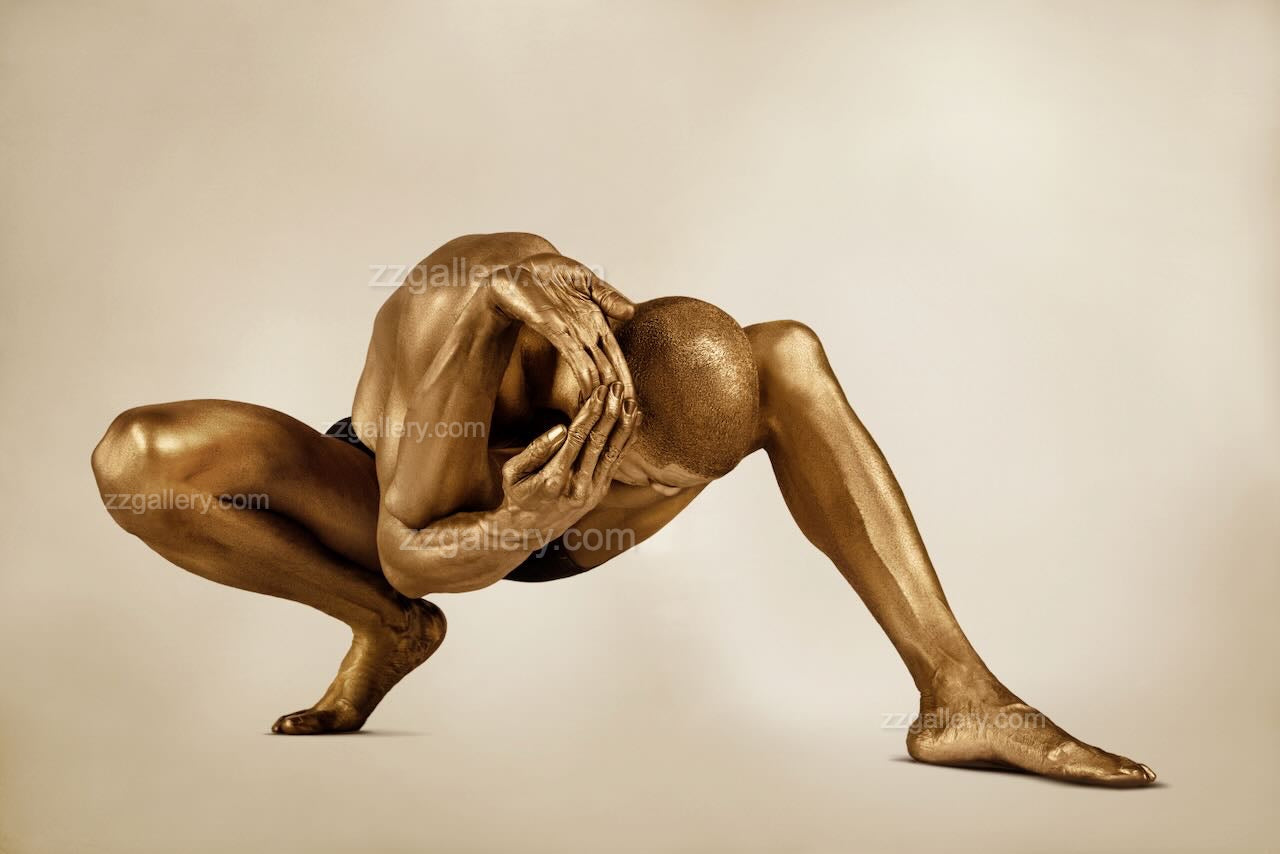 Golden-painted male in a crouched yogic pose, arms clasping head in introspection. Conceptual fine art photography by Zack Zublena, "The Wheel of Life."