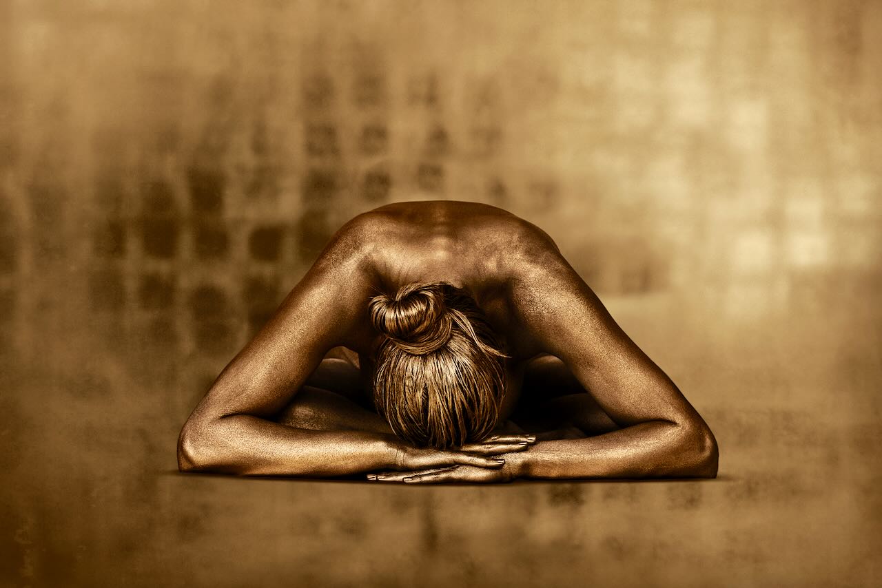Golden-painted woman in child’s pose on textured gold background – fine art photography by Zack Zublena, spiritual feminine wall art
