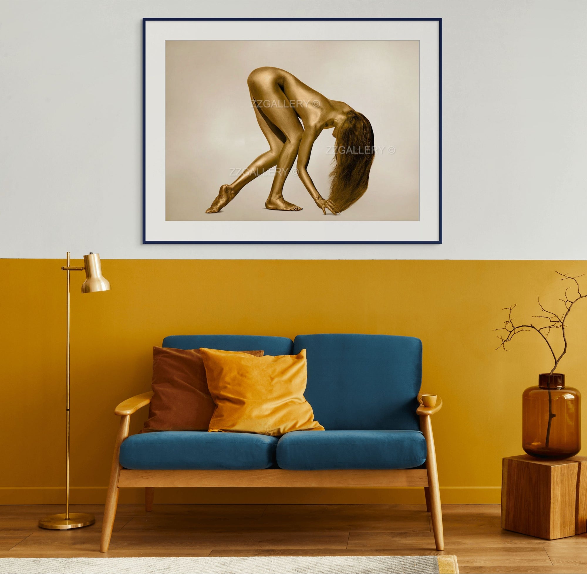 Golden-painted female figure in a sculptural pose displayed as luxury wall art above a modern blue and mustard sofa, blending elegance and contemporary interior design.