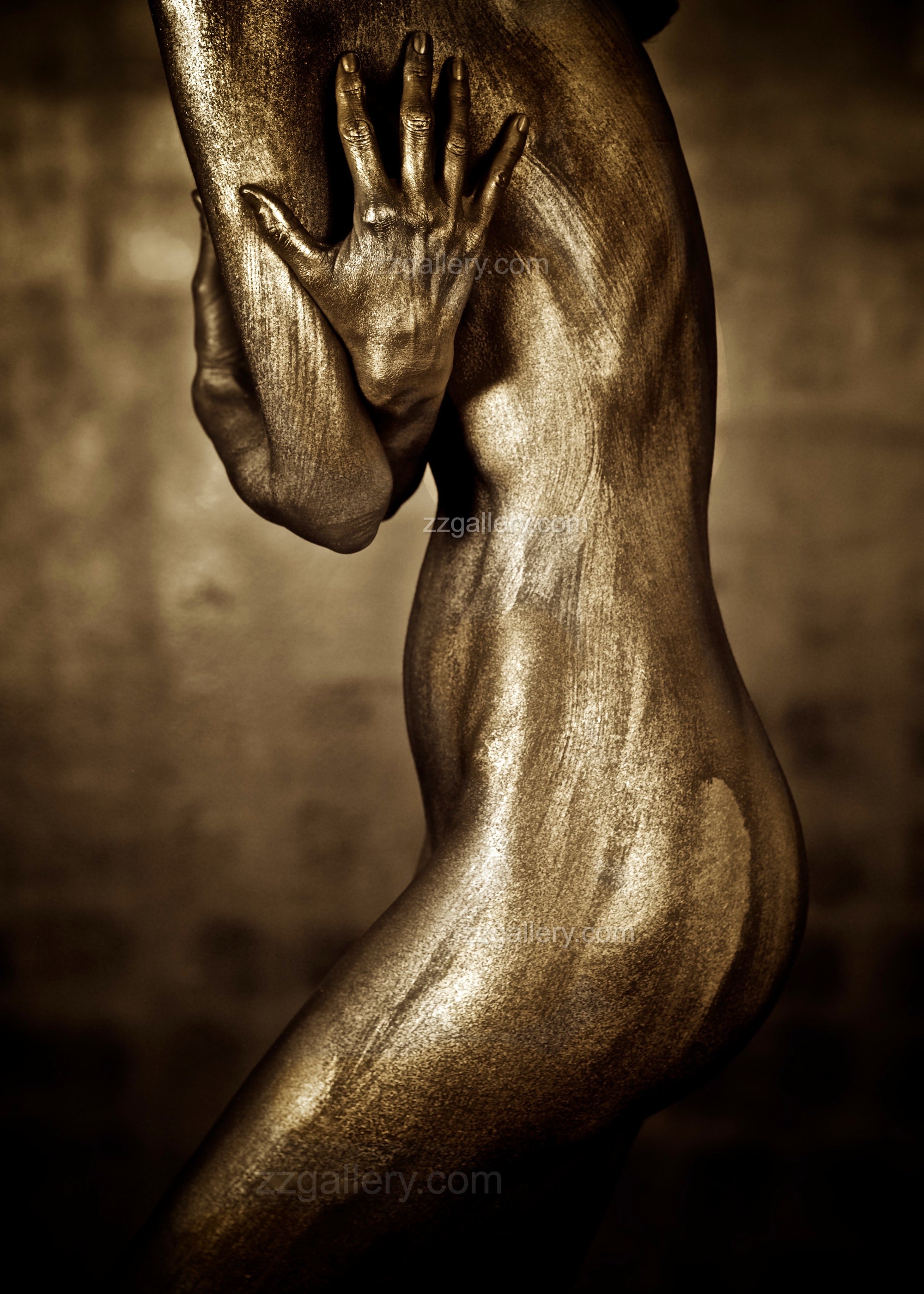 Golden female figure photographed from the side with protective hand gesture, fine art body photography in shimmering gold tones — contemporary sculptural wall art.