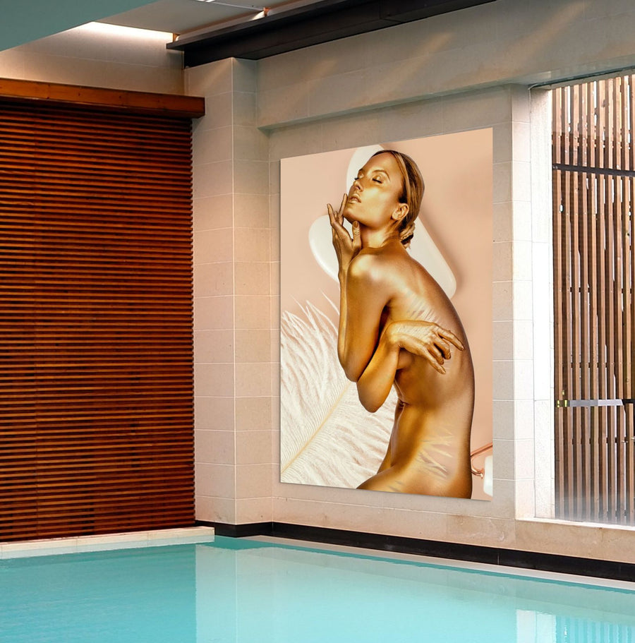 Golden-painted nude female figure in an elegant pose with soft feather background – luxurious fine art photography perfect for spa and wellness wall decor.