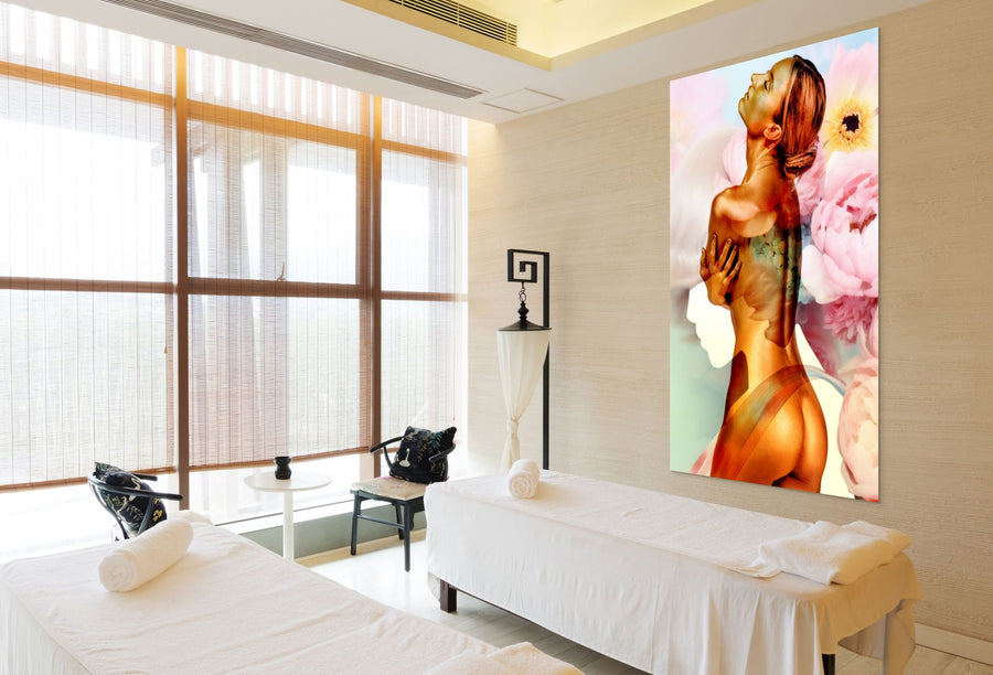 Golden nude female fine art photograph with floral background displayed in a serene spa treatment room with massage tables and natural light.