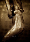 Golden-painted female silhouette in a sculptural pose with hand resting across her torso, fine art photograph emphasizing elegance, metallic tones, and refined contours.