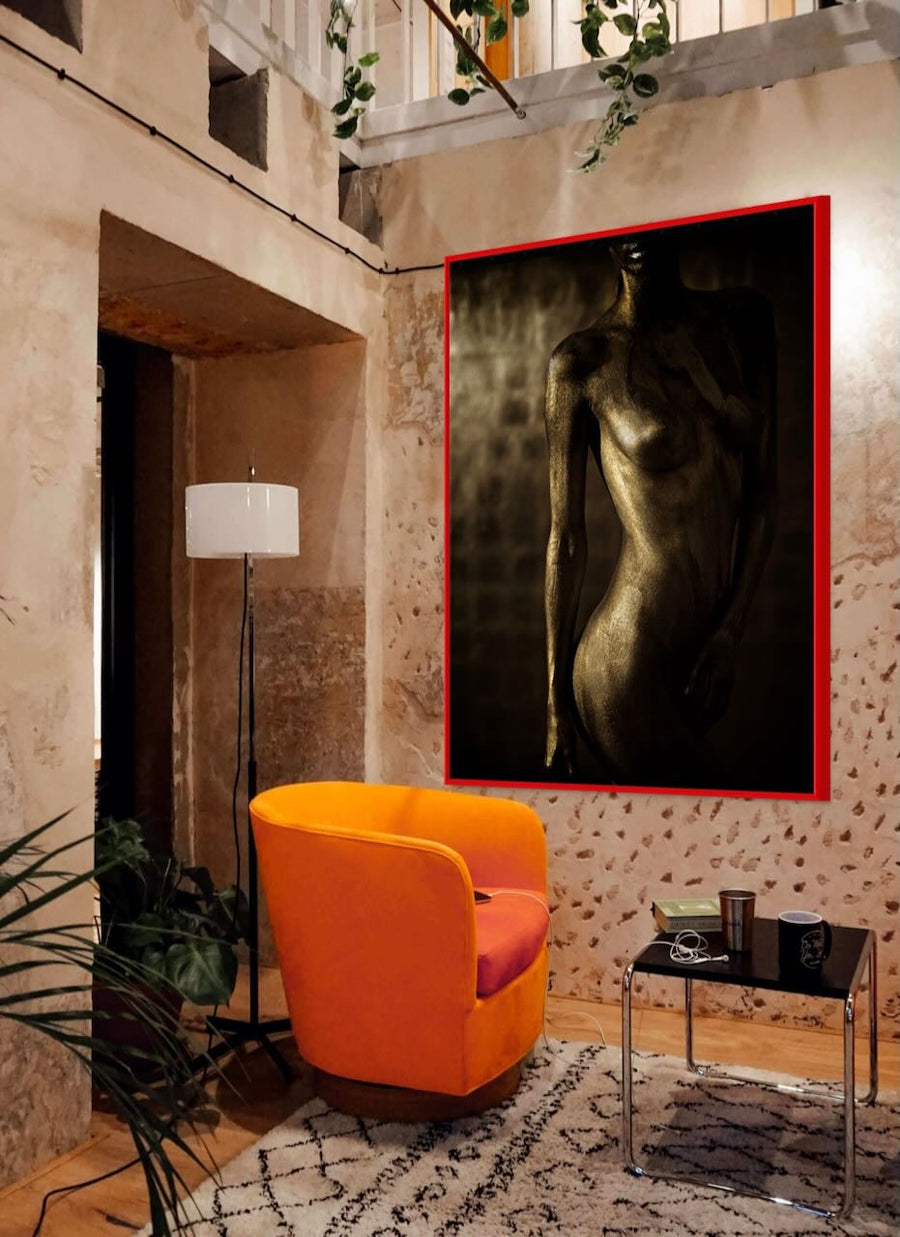 Golden-painted female silhouette artwork displayed on a textured stone wall in a rustic modern living room with a bright orange chair and cozy décor.