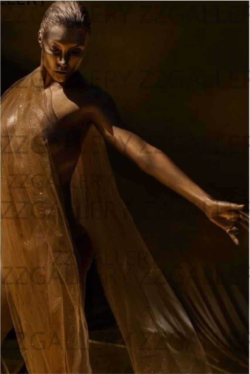 Golden figure in flowing fabric extending arm in dance-like pose, artistic shadow lighting.