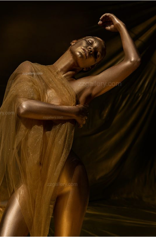 Figure painted in radiant gold, draped in sheer golden fabric, striking a graceful pose with arm raised above the head. Fine art photography emphasizing elegance and timeless beauty for interior wall decor.