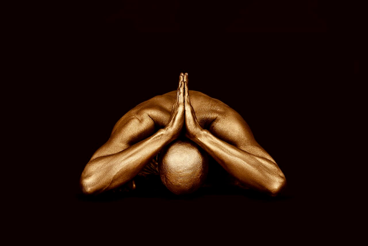 Gold-painted male figure bowing forward in a contemplative pose, fine art wall decor with dark background by Zack Zublena.