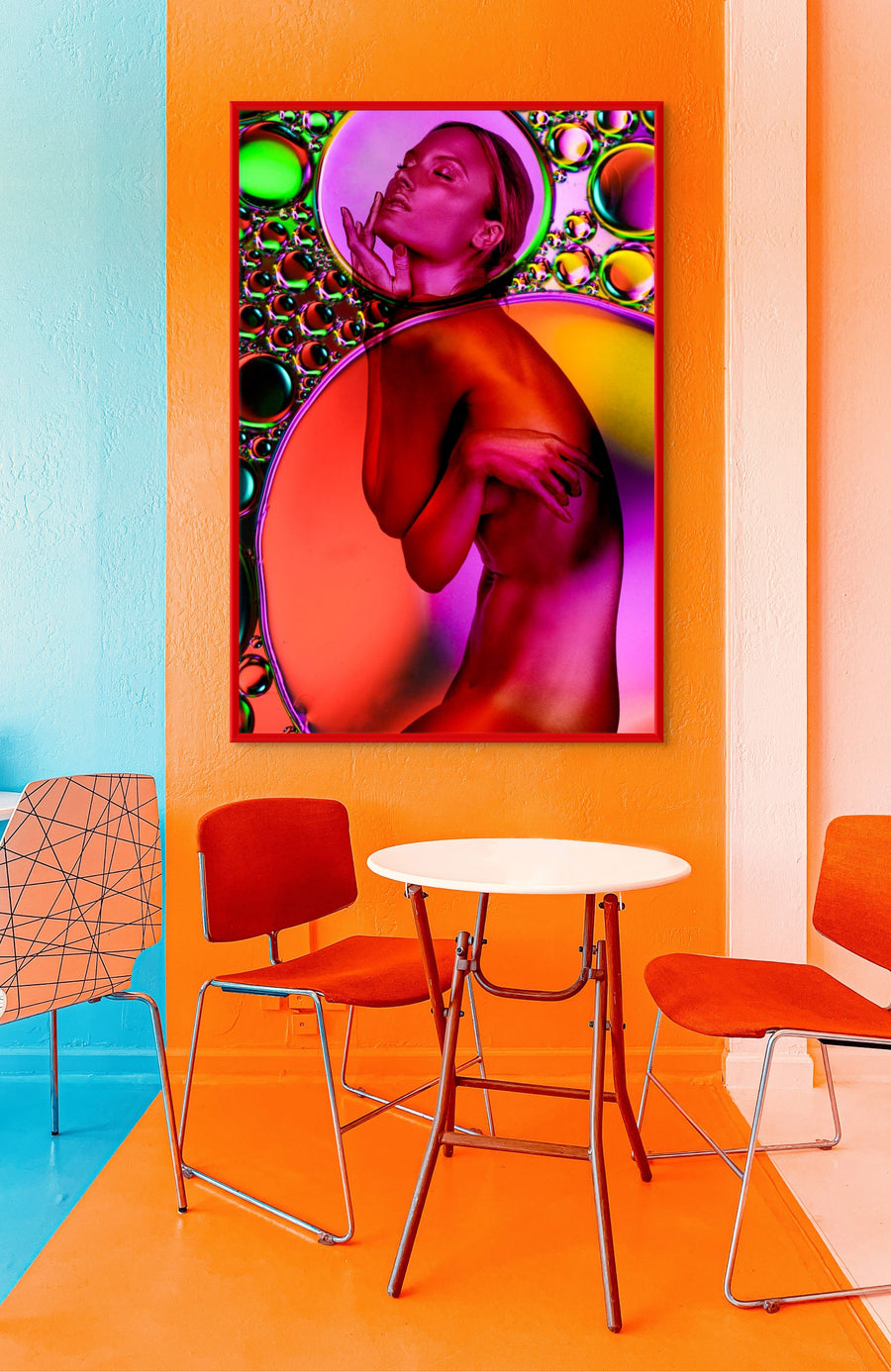 Colorful abstract painting on an orange wall above a small table and chairs.