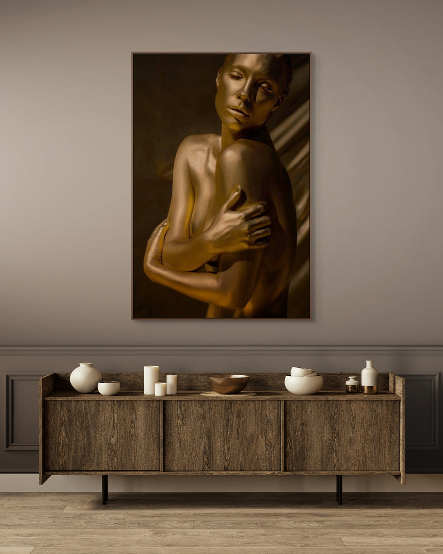 Elegant golden-painted figure with eyes closed and arms wrapped around shoulders, captured in warm light against a neutral background. Contemporary fine art photography symbolizing serenity, harmony, and timeless beauty — ideal for luxury interiors, spas, and collector wall art.