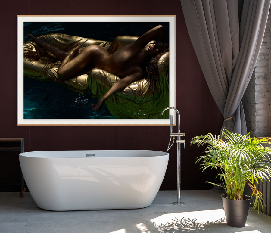 Golden-painted figure reclining on a shimmering gold float over deep blue water, illuminated dramatically to highlight elegant curves and textures. Luxurious fine art wall decor symbolizing freedom and refinement.
