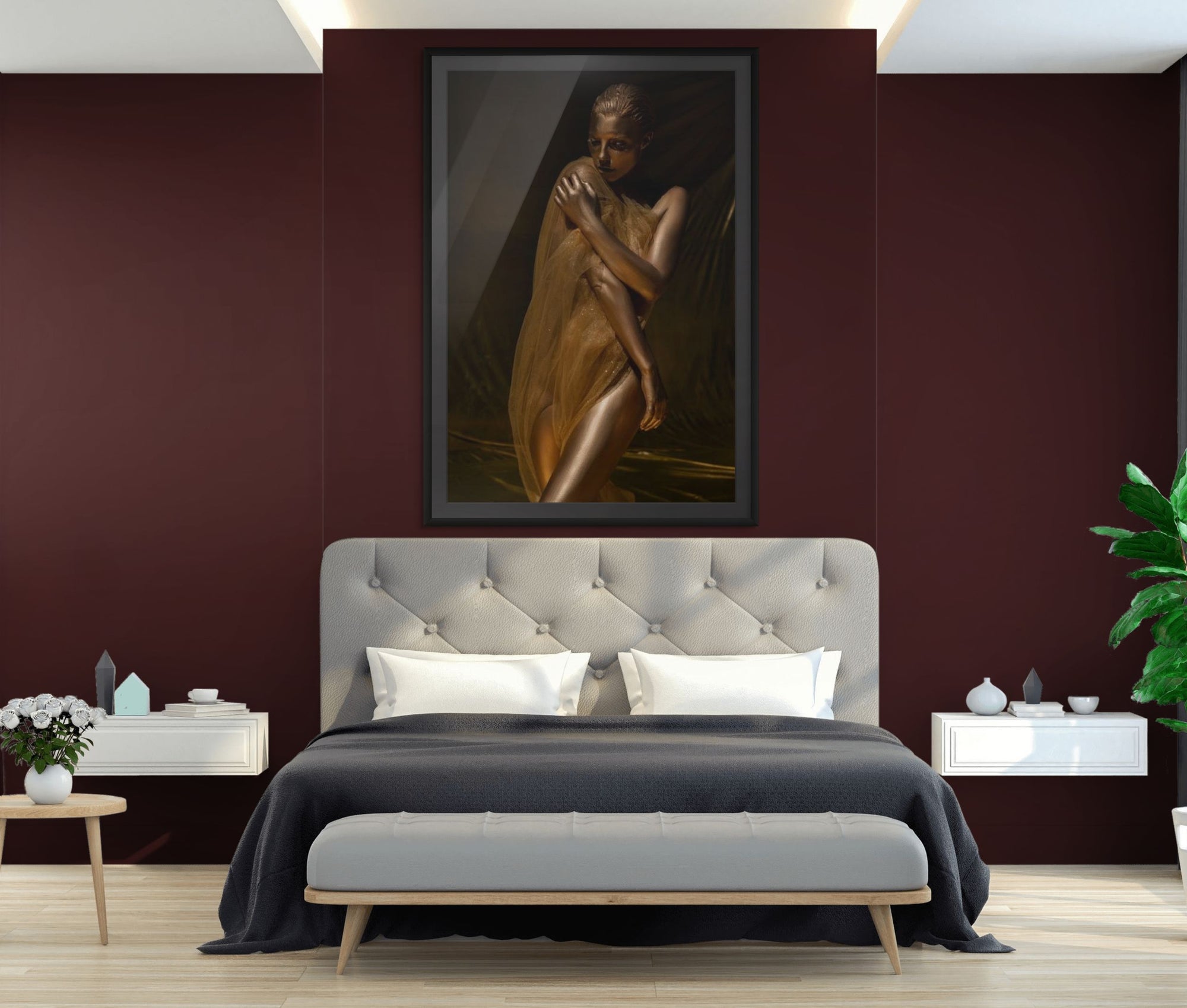 Framed golden fine art photograph of a woman with metallic body paint draped in sheer fabric, displayed above a modern bed with tufted headboard in a contemporary bedroom, elegant wall art for luxury interiors.