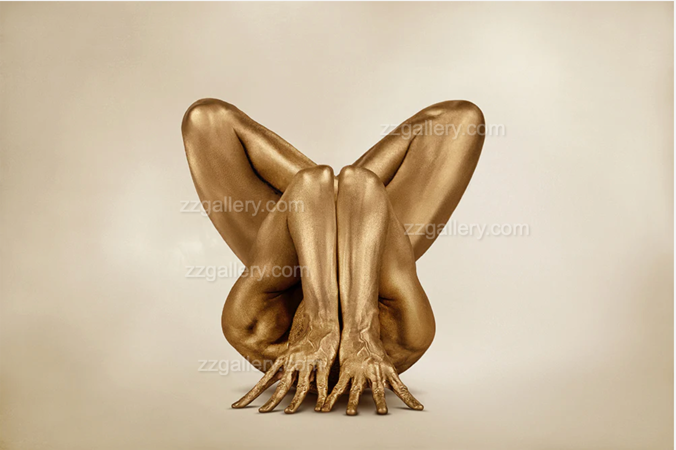 Gold-painted body folded in yoga lotus pose against beige background
