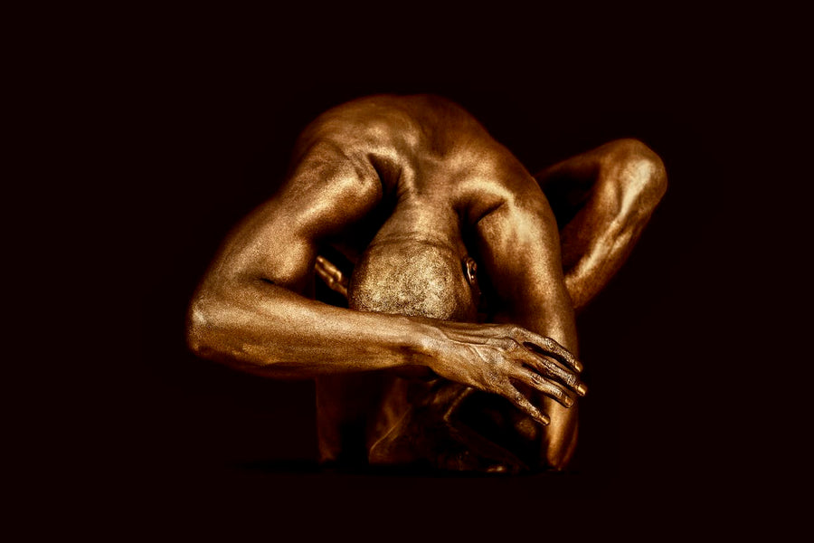 Golden-painted male figure in a sculptural contemplative yoga pose, fine art wall decor on a deep red background above a modern wooden console.