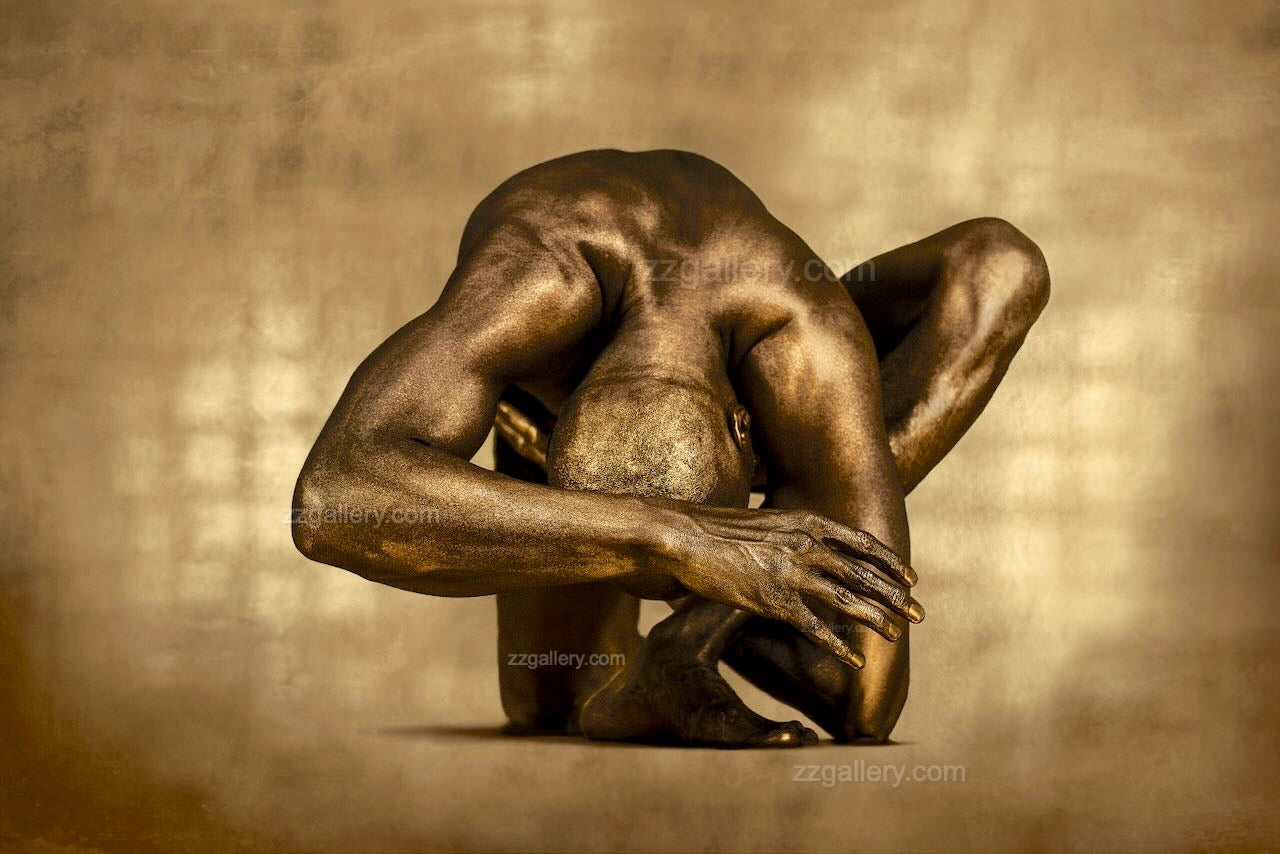 Golden male figure in fetal sculpture pose with rich textured background