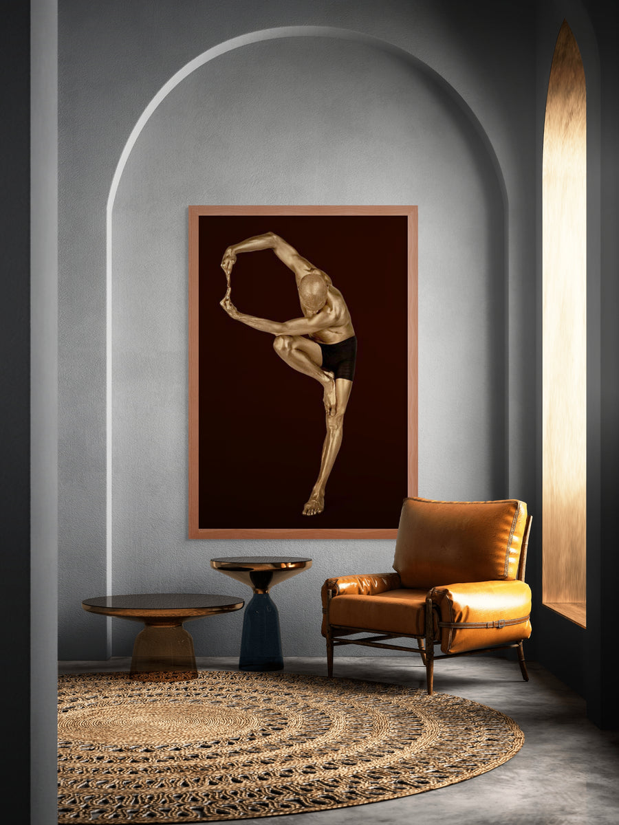 Golden-painted male dancer in a sculptural yoga balance pose, fine art wall decor displayed in a modern arched interior with leather chair and woven rug.